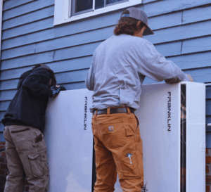 Two installers from Southern Energy install two franklin apower 2 battery systems outside a blue home