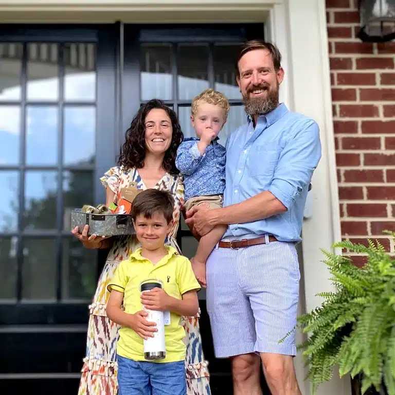 A family portrait of two parents with their children outside the front door of a home