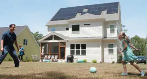 Family playing soccer in front of a home with a solar system