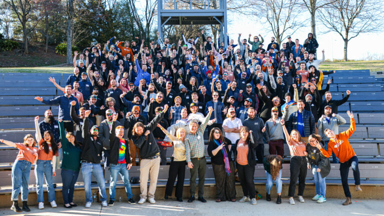 A large group of Southern Energy Management team members gathered on outdoor bleachers, smiling, cheering, and raising their hands in celebration