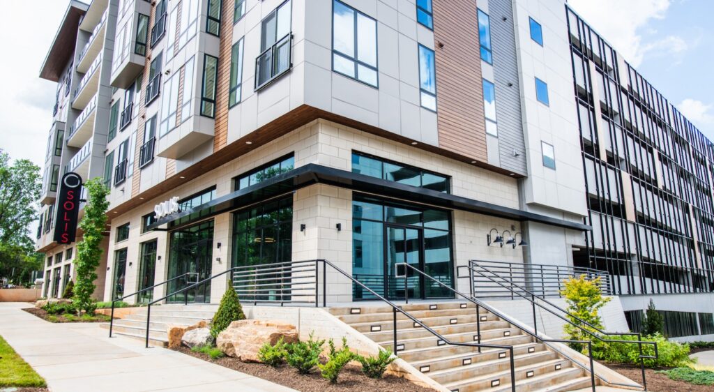 Entrance of Solis Midtown apartment complex with wide steps, landscaped areas, and a large glass facade, certified by Southern Energy Management for Fitwel and NGBS Silver.