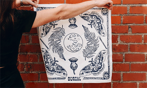 A white bandana with navy illustrations of ferns, the moon, moths, and natural elements from Burial Beer Co