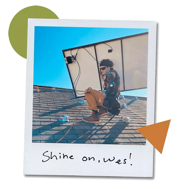 Solar Installer, Wes, on a roof holding a solar panel while pointing a drill at the camera