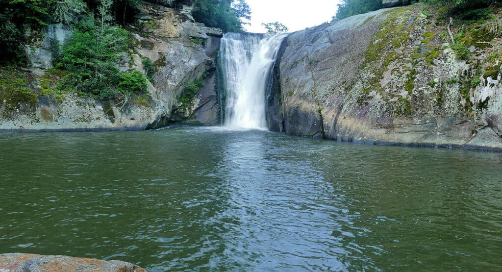 Elk River Falls cascades powerfully between weathered rock faces into a broad, tranquil pool, surrounded by dense greenery