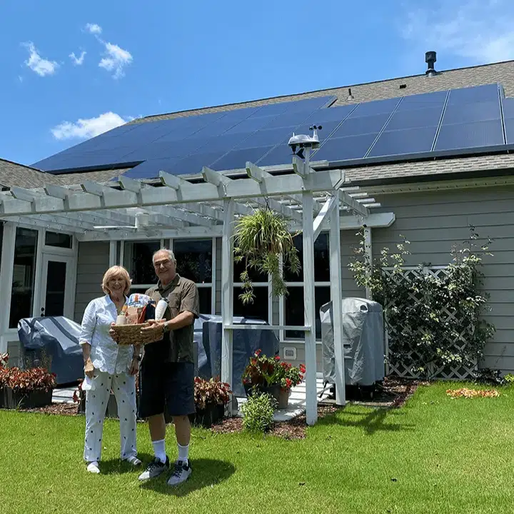 John and Lucy standing out side in front of their rooftop solar system and holding the raffle prize