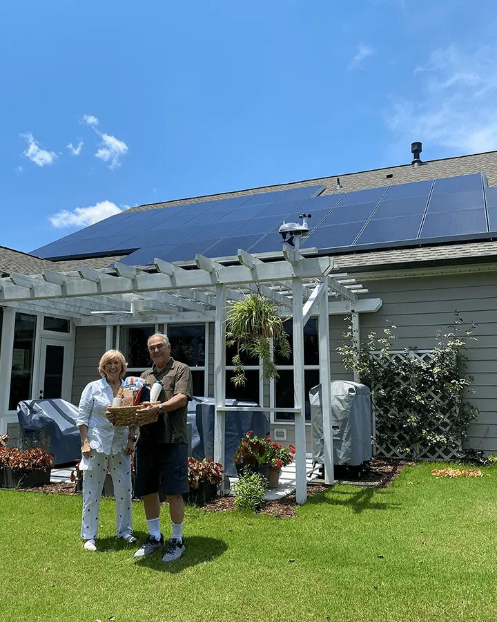 John and Lucy standing out side in front of their rooftop solar system and holding the raffle prize
