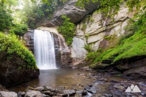 Looking Glass Falls dramatically plunges from a cliff into a serene pool below, surrounded by rock walls and vibrant greenery, displaying its majestic flow