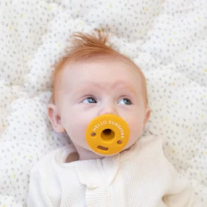 infant with a golden pacifier that says hello sunshine in its mouth from Bella Tuno