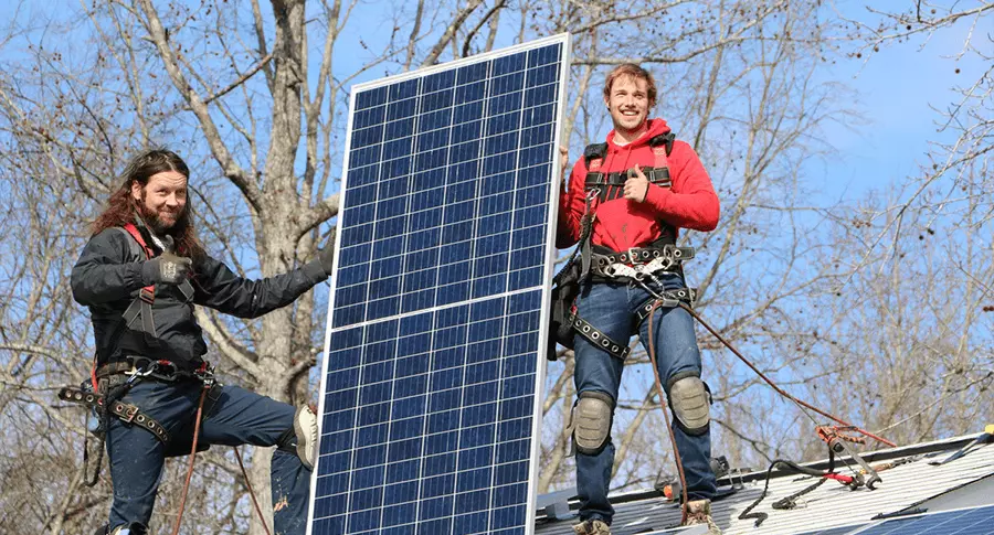 Two solar installers giving a thumbs up while they hold a solar panel on a roof
