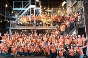 a group photo of the team at southern energy management wearing orange shirts in an industrial space and cheering with joy
