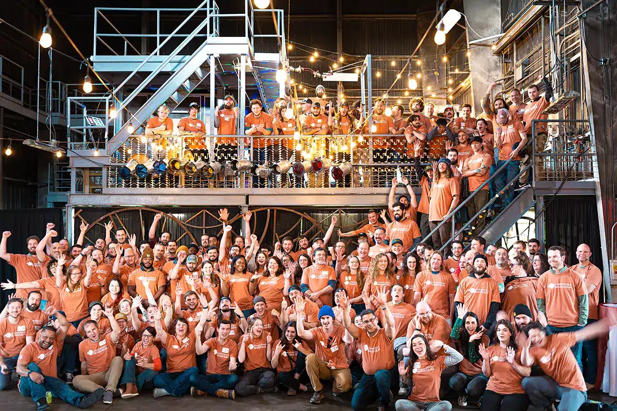 a group photo of the team at southern energy management wearing orange shirts in an industrial space and cheering with joy