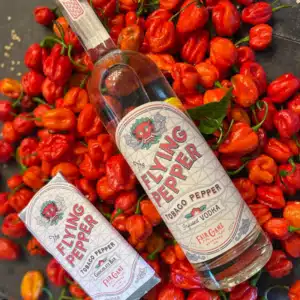 bottle of flying pepper vodka laying on top of peppers from Fair Game Beverage Co