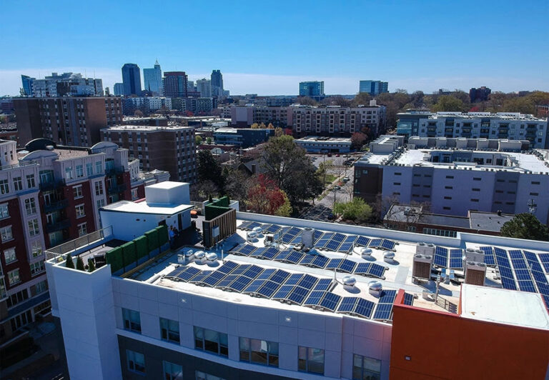 Drone shot of a multifamily complex with solar panels installed on the rooftop against the backdrop of a city skyline